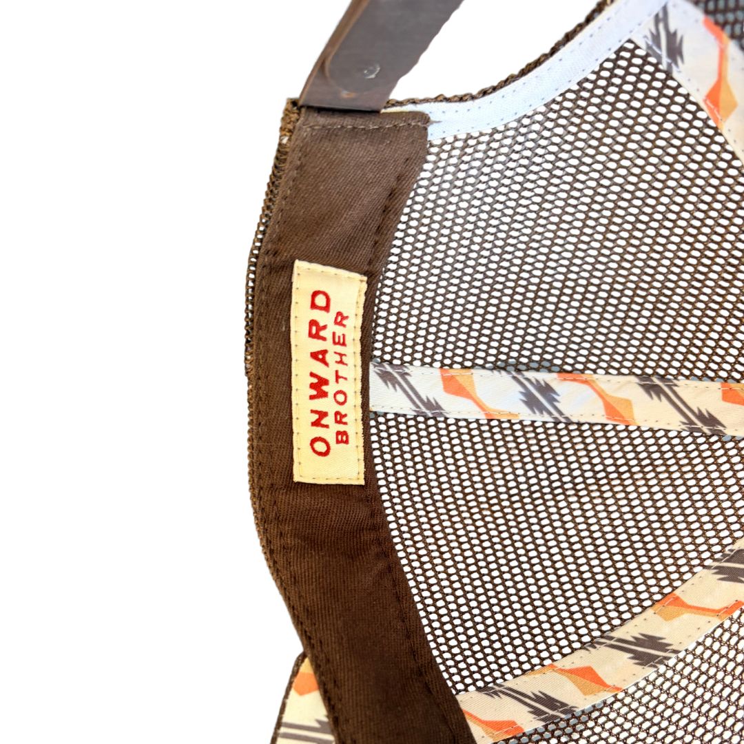 Close-up of the back strap and mesh backing of a cap, showing a brown fabric strap with a beige label that reads 'ONWARD BROTHER' in red text, and a patterned orange, black, and white mesh section.