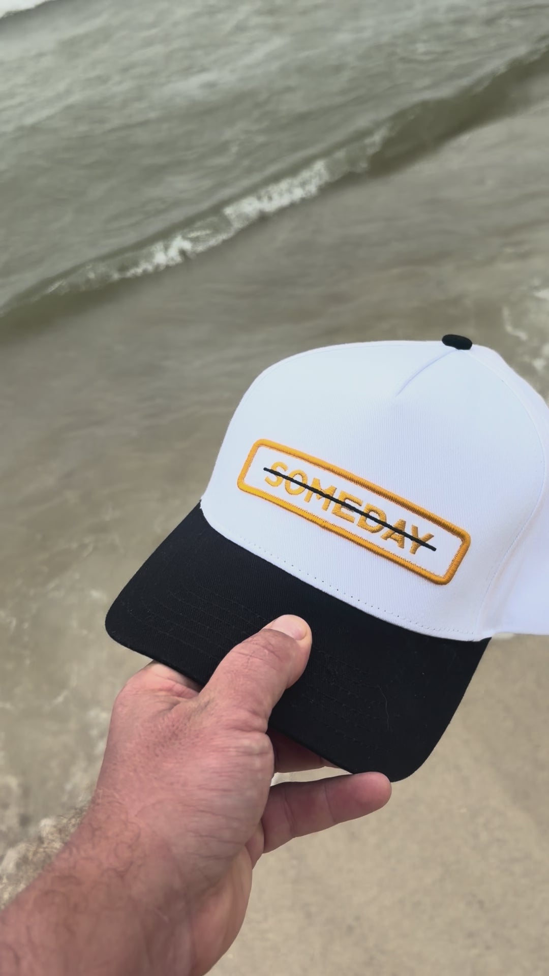 video of the "someday" hat, with the word crossed out being shown with the ocean in the background.