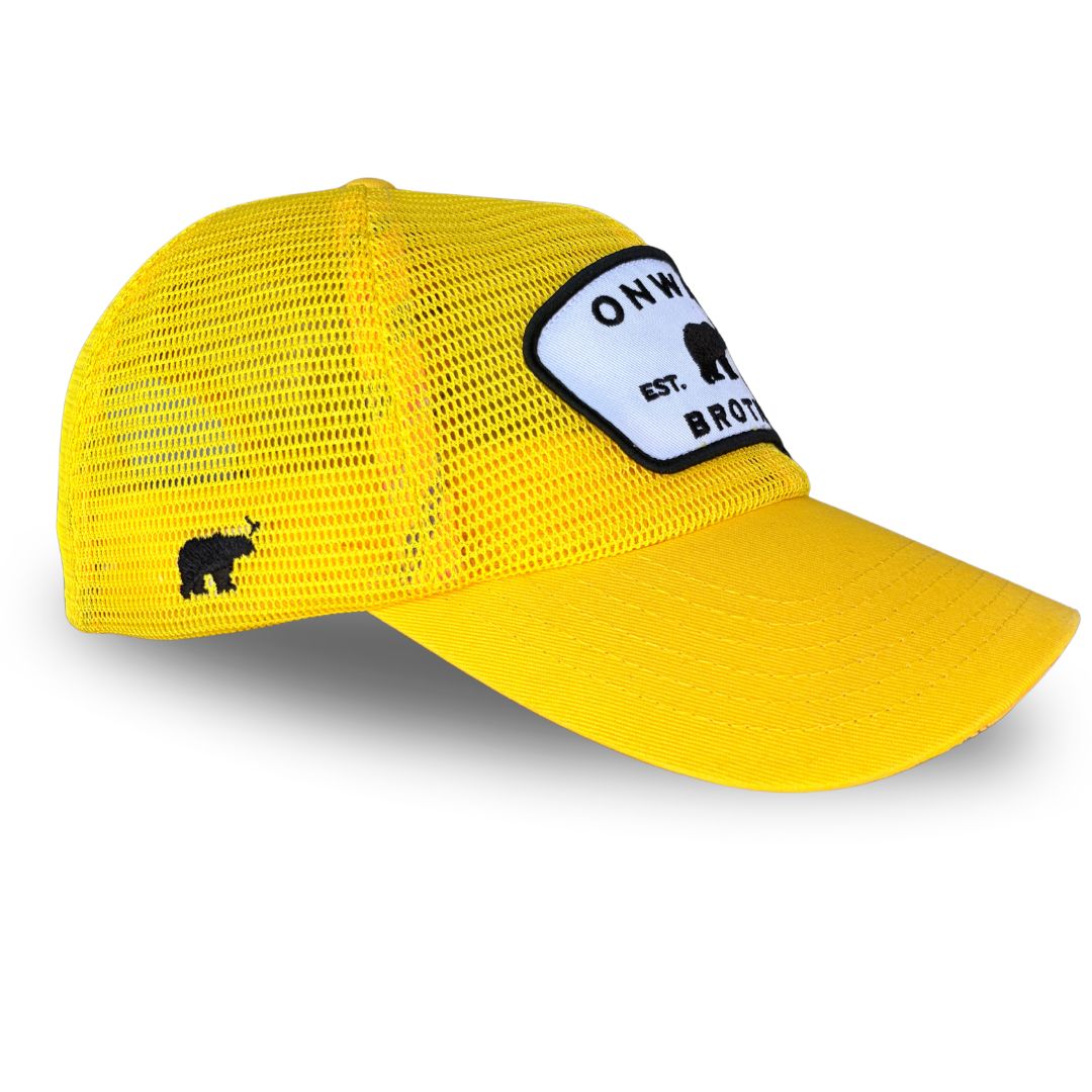A bright yellow trucker hat with a white and black embroidered patch on the front that reads 'ONWARD BROTHER, est day 6' with a black bear silhouette. Side view.