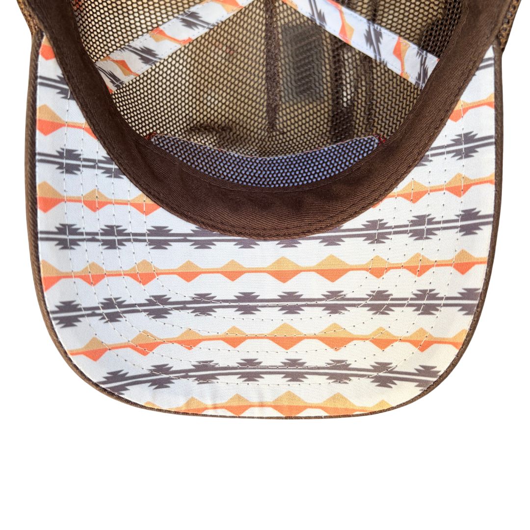 Close-up of the underside of a trucker-style cap showing a white brim with a brown, gray, and orange geometric pattern, a brown mesh back, and a brown fabric lining.