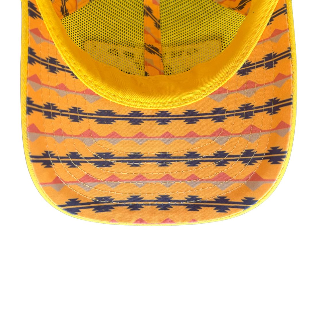 Close-up of the front brim of a yellow baseball cap with a geometric Southwestern pattern in navy blue, orange, and gray, featuring a yellow mesh back.