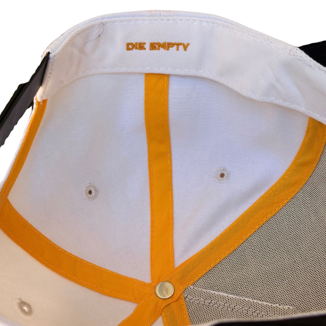 Close-up of the inside crown of a white baseball cap with mustard yellow trim and the brand name 'DIE EMPTY' embroidered in yellow on the white crown.